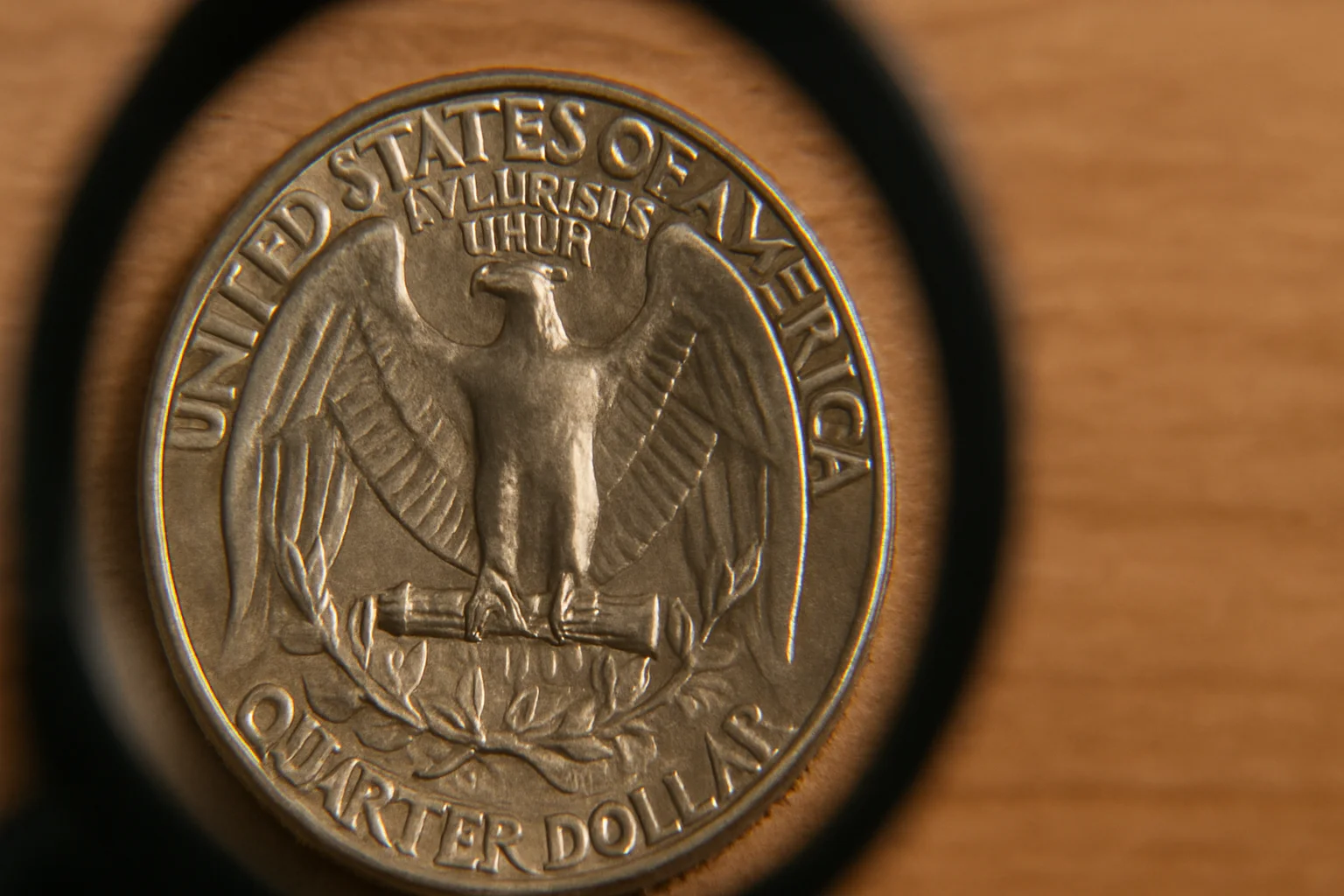Close-up of a U.S. quarter under a magnifying glass, showing the eagle reverse design in sharp detail on a wooden surface.